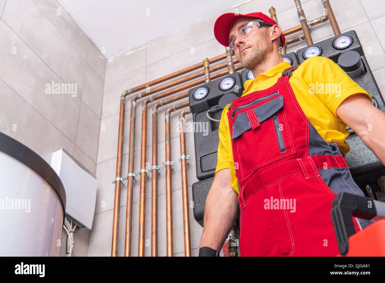 Idraulico caucasico nel suo lavoro uniforme in piedi nel mezzo del reparto bollitura tecnica pronto per controllare e riparare il sistema di tubazioni. Tecnici sanitari Foto Stock