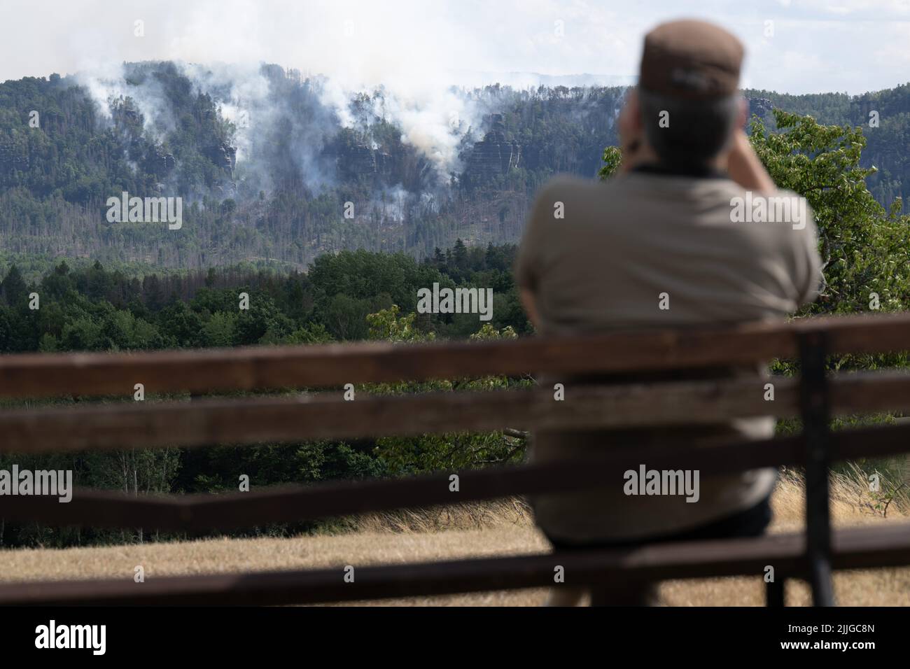 Schmilka, Germania. 26th luglio 2022. Un uomo su una panchina con binocolo osserva un incendio nel Parco Nazionale della Svizzera Sassonia. Nel caso di un incendio forestale nel Parco Nazionale della Svizzera Sassonia, il distretto colpito ha emesso un allarme per il disastro di Bad Schandau. Credit: Sebastian Kahnert/dpa/Alamy Live News Foto Stock