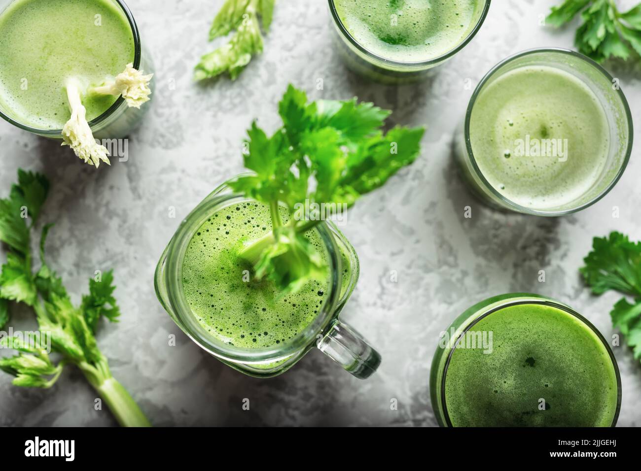 Succo di sedano fresco verde in bicchieri diversi su tavola grigio arrugginito. Sfondo sano di cibo vegetariano Foto Stock