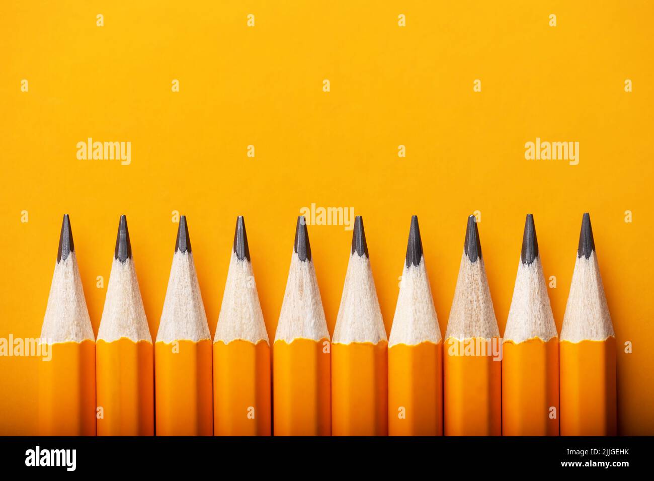 Sfondo astratto di matite gialle che giacciono in una fila. Concetto di colore giallo e arancione Foto Stock