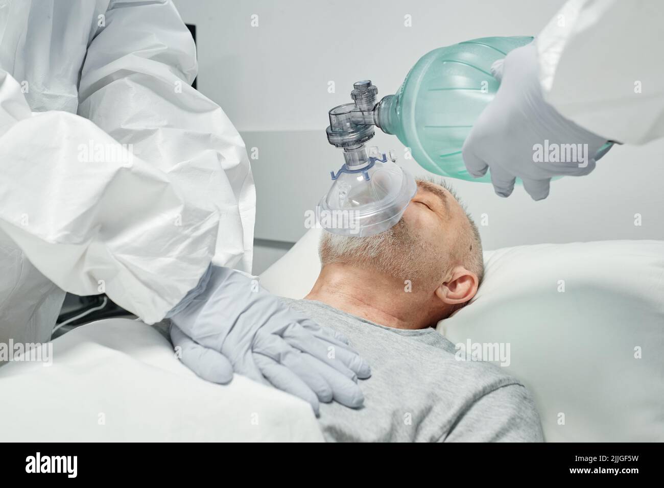 Lavoratori medici professionisti non riconoscibili che indossano dispositivi di protezione personale che eseguono la RCP per l'uomo maturo Foto Stock