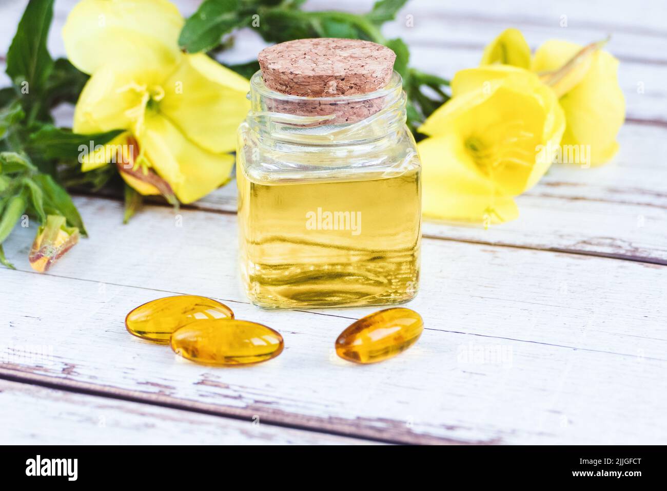 Sera olio di primrose in bottiglia, pillole e fiori su tavola di legno, essenza di biennis Oenotha Foto Stock