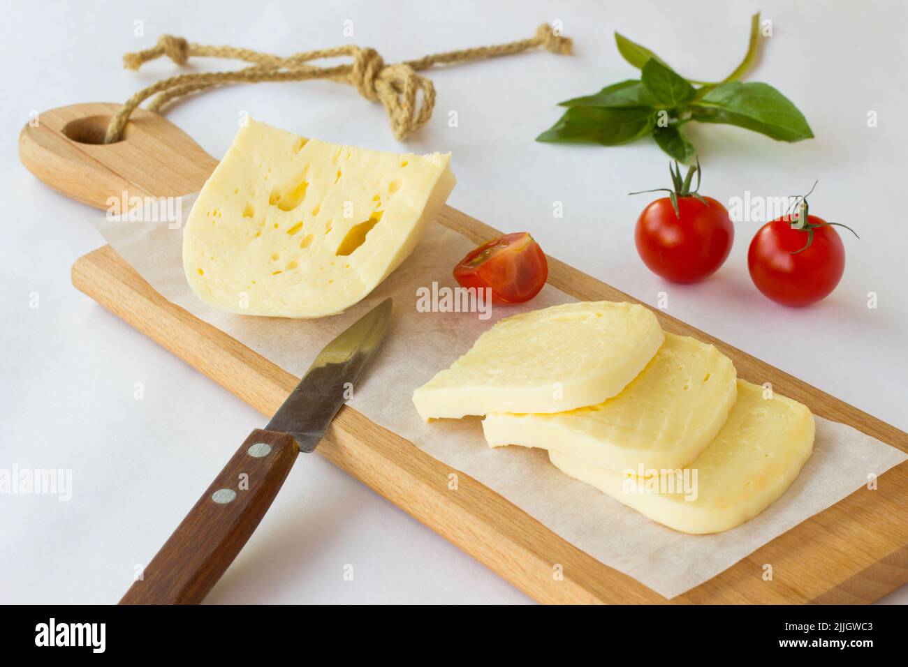 Formaggio a fette, pomodori e basilico verde su un tagliere Foto Stock