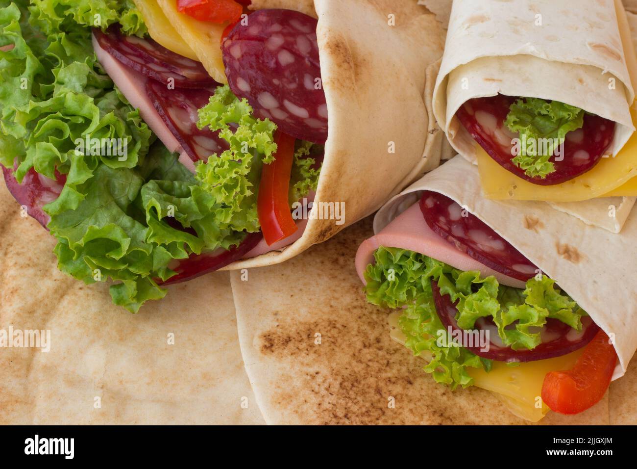 Arrotolate la tortilla con le erbe, il formaggio e la carne su uno sfondo bianco. Primo piano Foto Stock