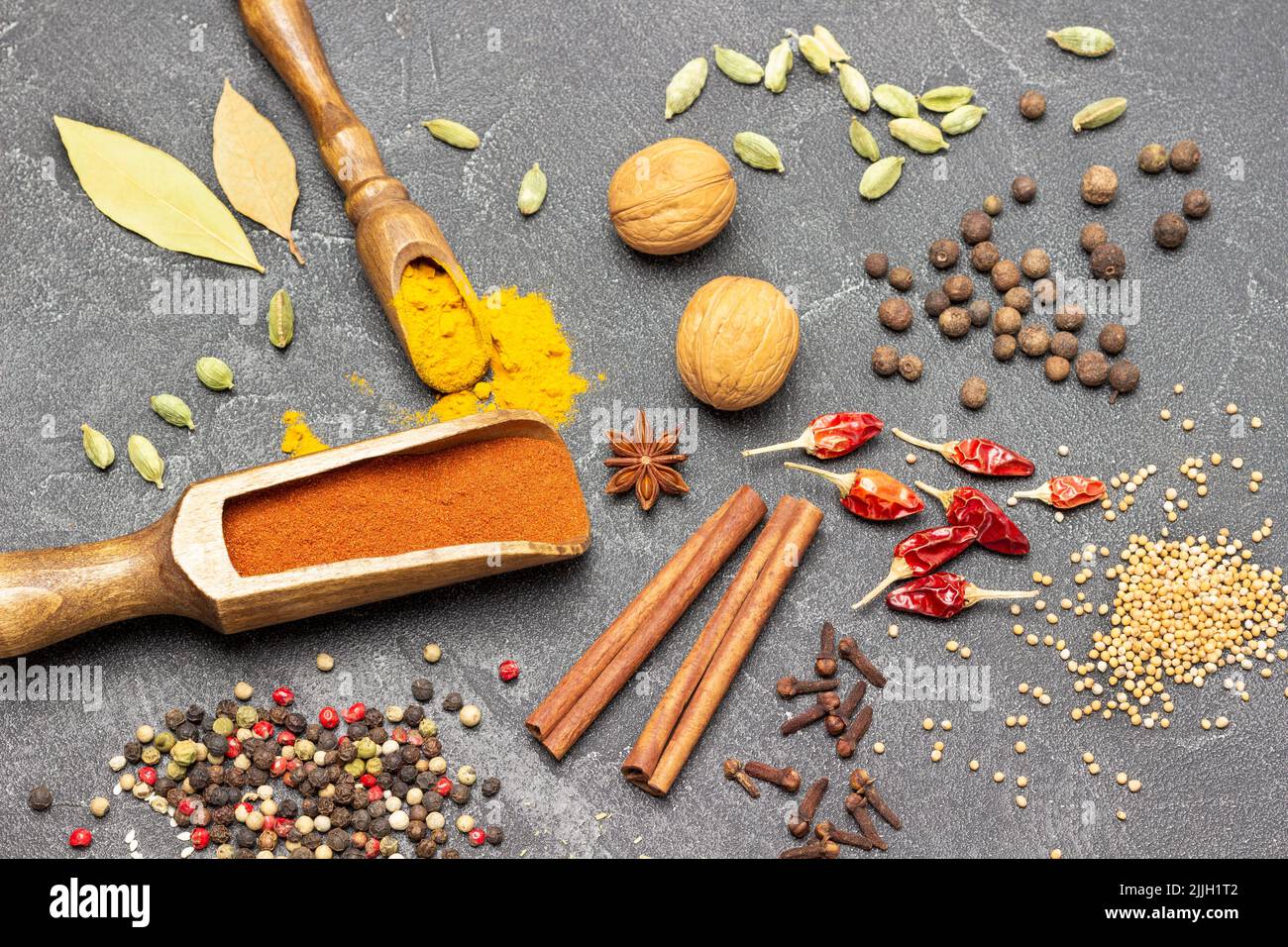 Noci, paprika macinata in ciotola e scoop. Bastoncini di cannella, cialde di peperoni rossi e spezie. Disposizione piatta. Sfondo nero Foto Stock