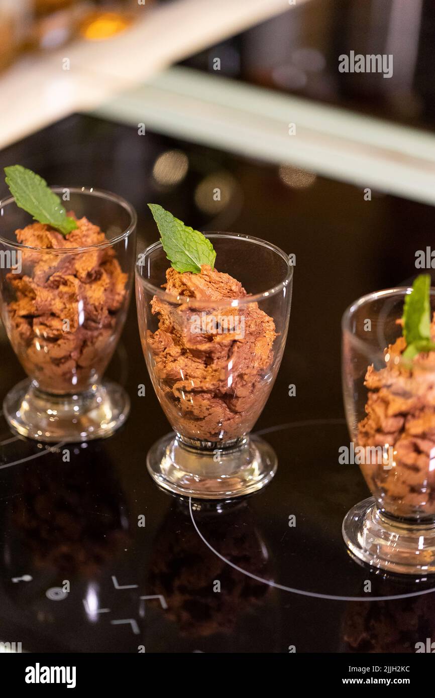 Un ritratto di alcune tazze di vetro pieno di deliziosa mousse di cioccolato con una foglia di menta sopra di loro per una certa freschezza in piedi su un piatto di cottura pronto Foto Stock