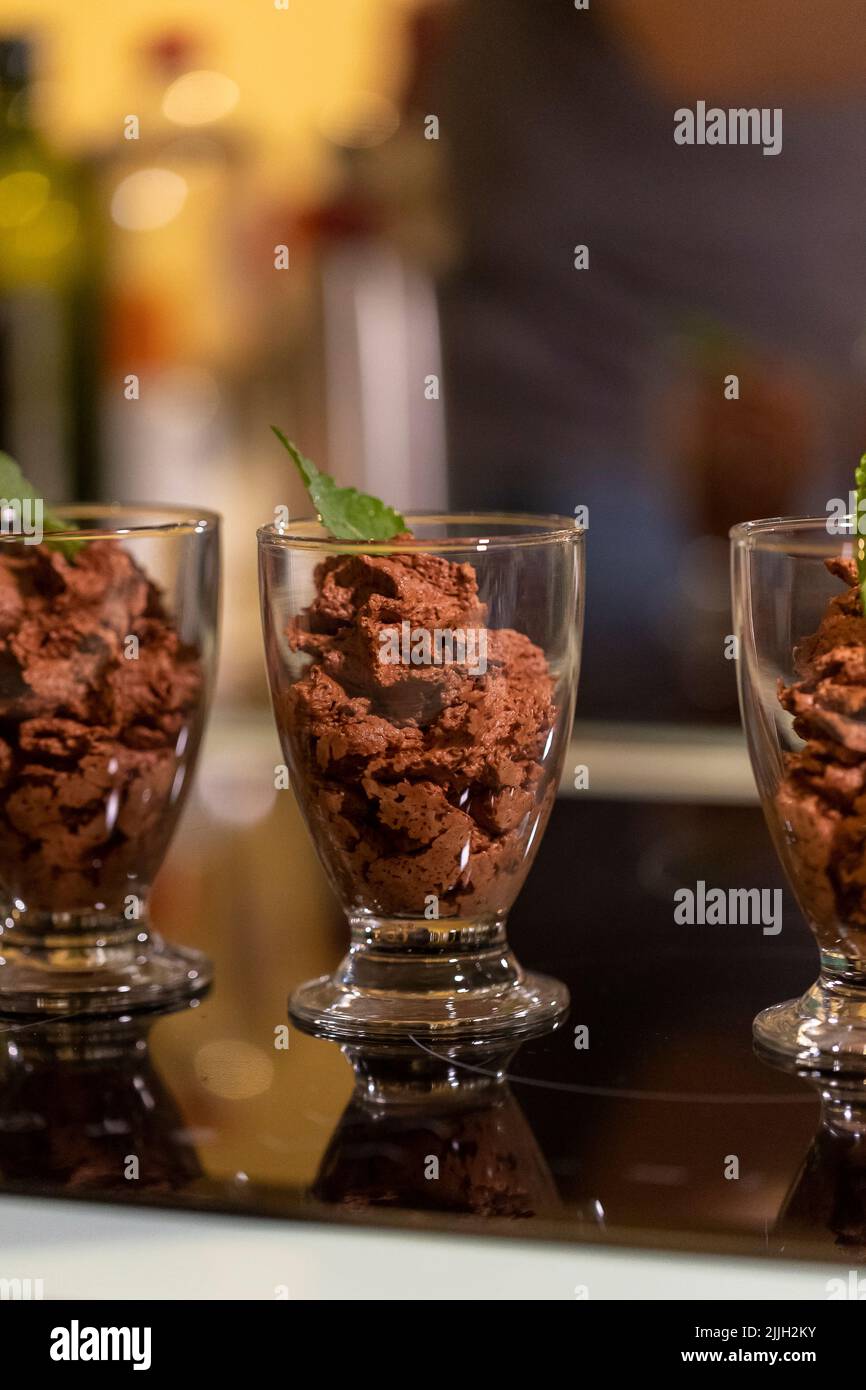 Un ritratto da vicino di alcune tazze di vetro piene di deliziosa mousse di cioccolato con una foglia di menta sopra di loro per una certa freschezza in piedi su un pl di cottura Foto Stock