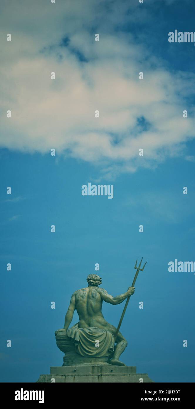 Un colpo verticale della statua del dio Nettuno con un tridente sotto un cielo blu Foto Stock