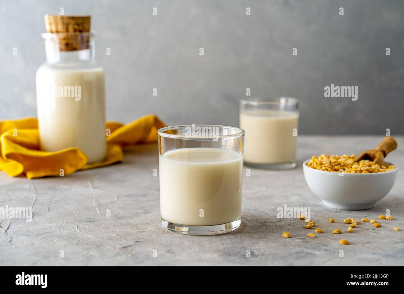 Vegano sano latte di piselli in bottiglia di vetro e due bicchieri, fondo in cemento, grani di piselli, tovagliolo giallo. Spazio di copia Foto Stock
