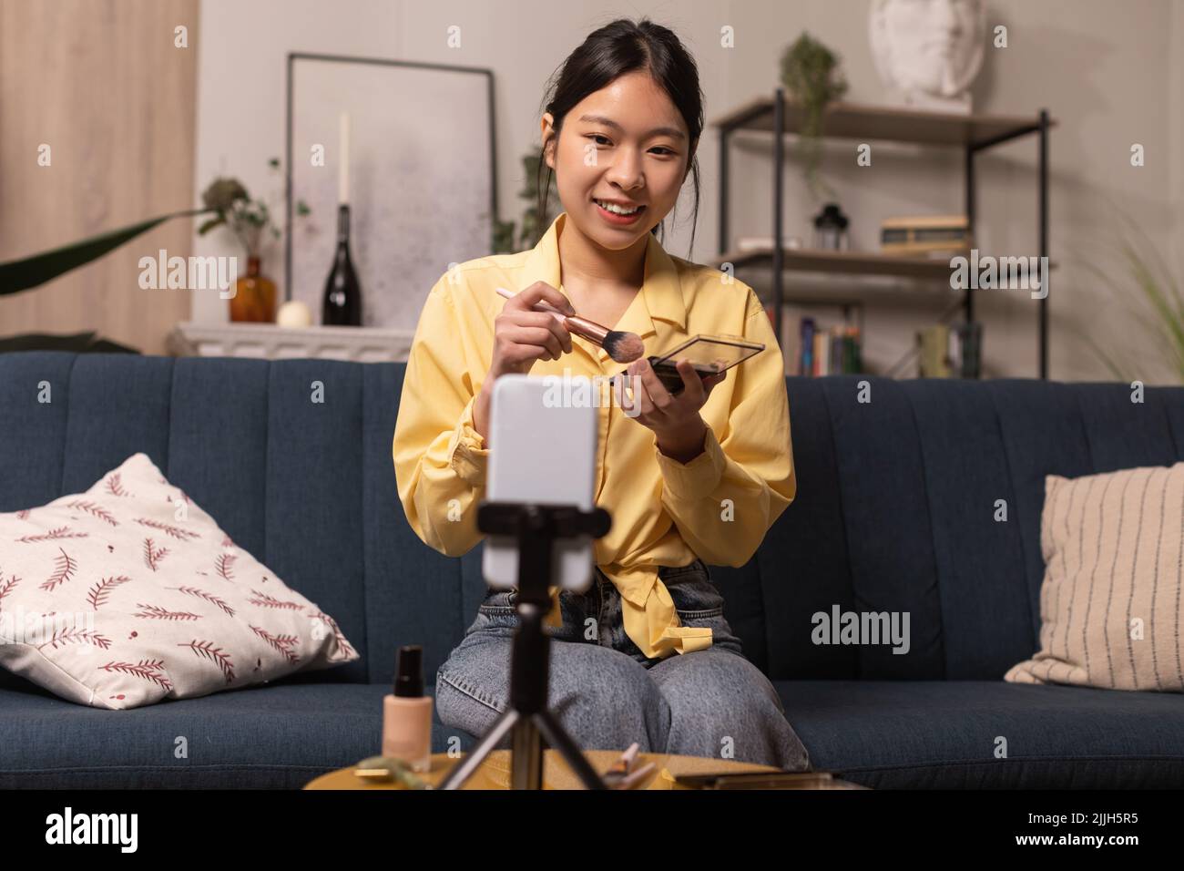 Asian Female Blogger fare Makeup filma su cellulare a casa Foto Stock