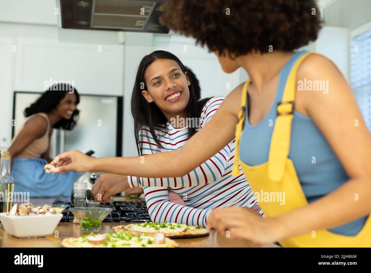 Giovane donna biraciale sorridente che guarda l'amico mentre prepara la pizza sull'isola della cucina a casa Foto Stock