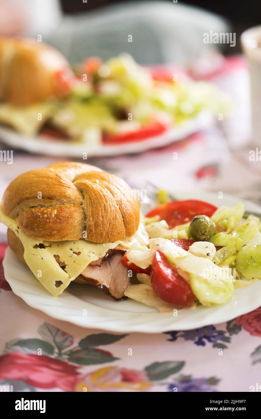 Panino fresco con prosciutto e formaggio e insalata estiva con lattuga, pomodori, formaggio feta Foto Stock