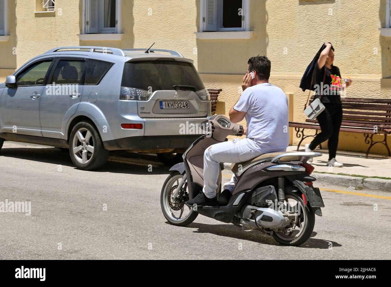 Argostili, Cefalonia, Grecia - Giugno 2022: Ho una persona che guida uno scooter a motore mentre uso un telefono cellulare Foto Stock