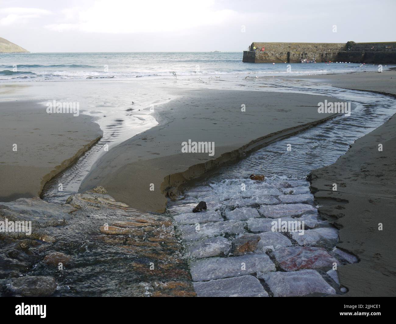 Acciottolati sotto la sabbia dove il torrente incontra il mare al Porto di Gorran Haven Foto Stock