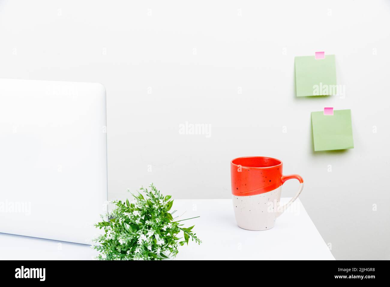 Uno spazio di lavoro ordinato con un computer portatile, note appiccicose sulla parete, una pianta e una tazza Foto Stock