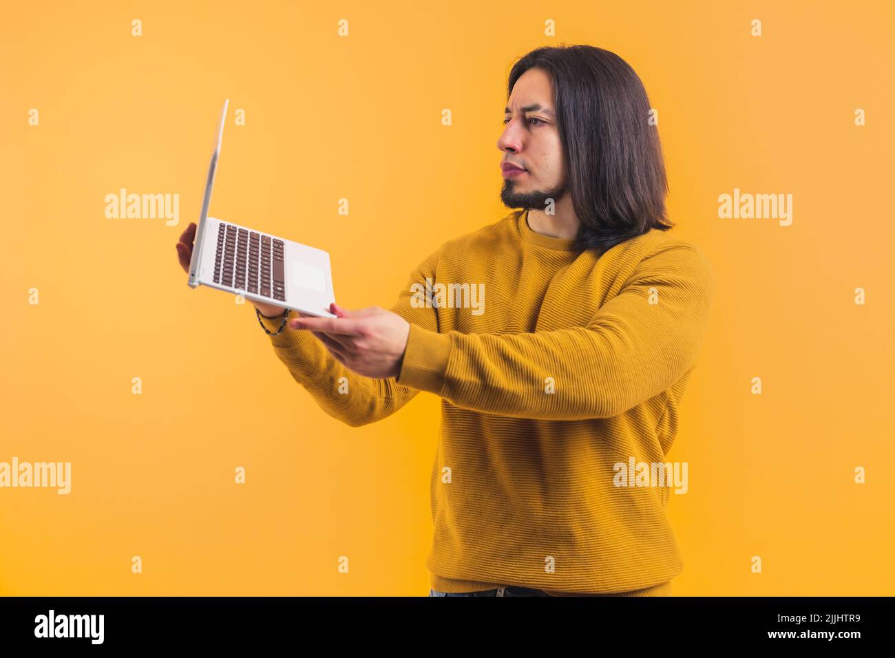 Giovane uomo portico che indossa un maglione arancione che tiene un notebook all'interno di una stanza su uno sfondo. Foto di alta qualità Foto Stock