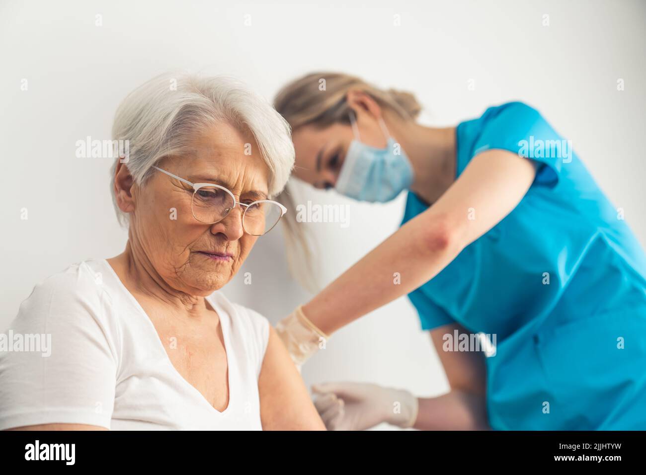Giovane infermiera che fa l'iniezione di farmaco o vaccino anti-covid ad una donna anziana con capelli grigi all'ospedale. Foto di alta qualità Foto Stock
