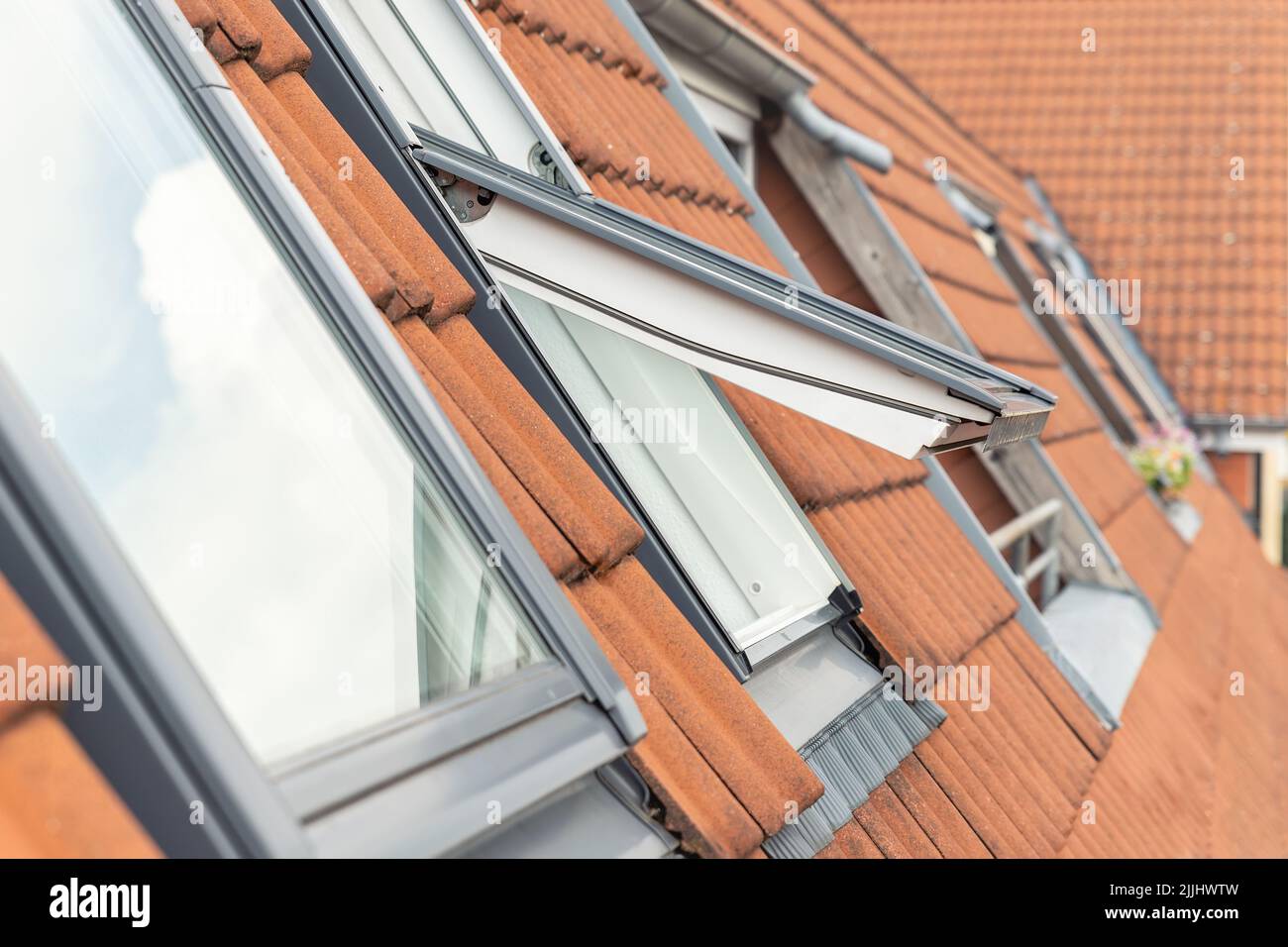 Ventilazione all'aperto impermeabile finestra tetto esterno contro luce solare cielo. Tetto in stile VELUX con mattonelle in mattoni rossi. Mansarda sottotetto di strada europea Foto Stock