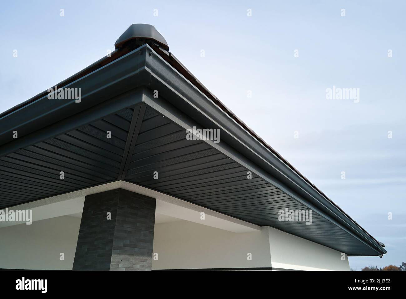 Angolo della casa con tavolette in metallo marrone e tetto con sistema di pioggia grondaia in acciaio. Installazione di coperture, costruzioni, tubi di drenaggio Foto Stock
