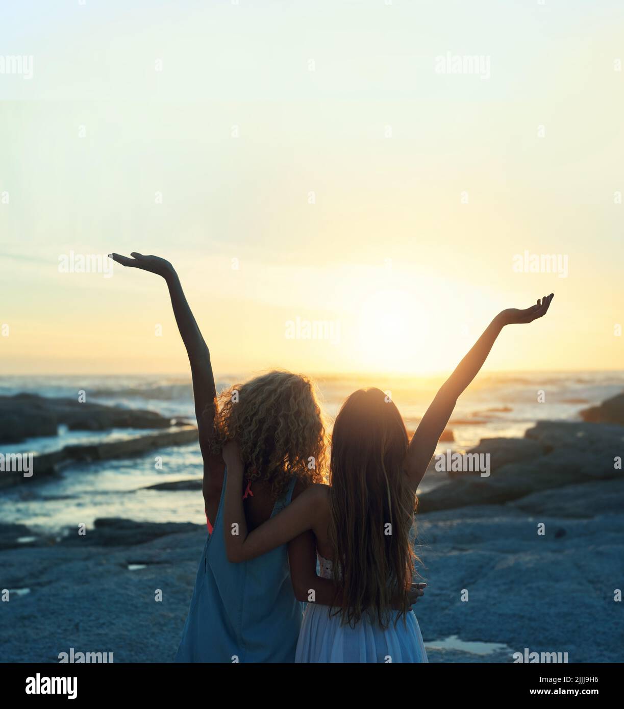 due amiche sulla spiaggia festeggiano con le braccia sollevate guardando al tramonto godendo di libertà di viaggio stile di vita Foto Stock