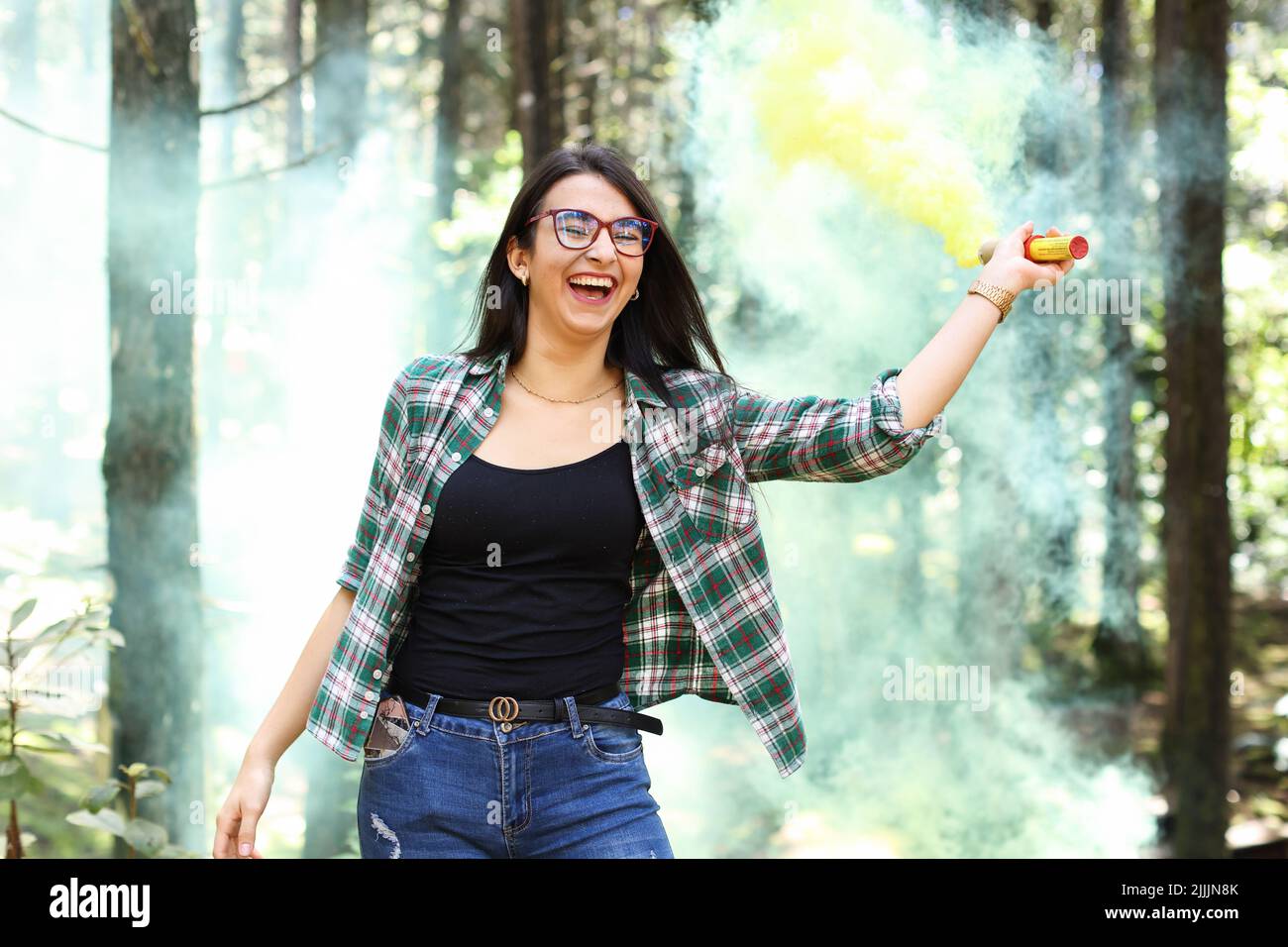 Giovane donna in un photoshoot alzando la sua mano tenendo una bomba di fumo giallo nella foresta sorridendo in Costa Rica Foto Stock