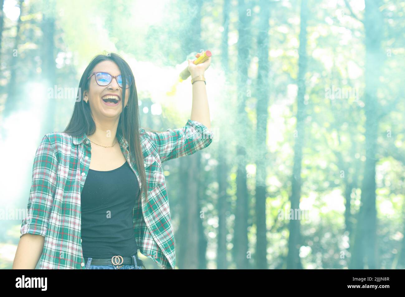 Giovane donna in un photoshoot alzando la sua mano tenendo una bomba di fumo giallo nella foresta sorridendo in Costa Rica Foto Stock