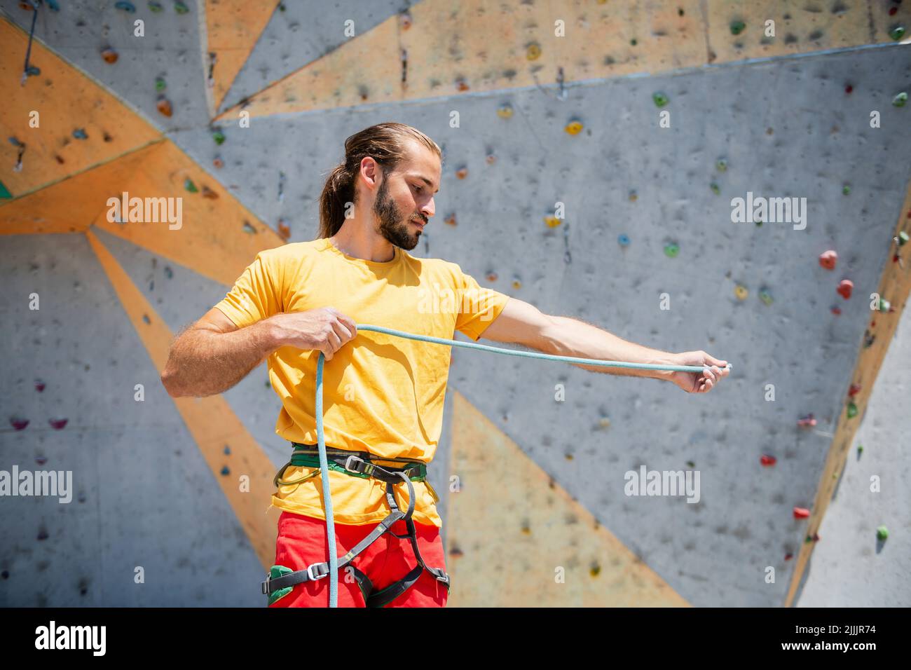 L'arrampicatore sportivo si prepara a salire su un percorso di arrampicata, arrampicandosi su una parete artificiale all'aperto. Foto Stock