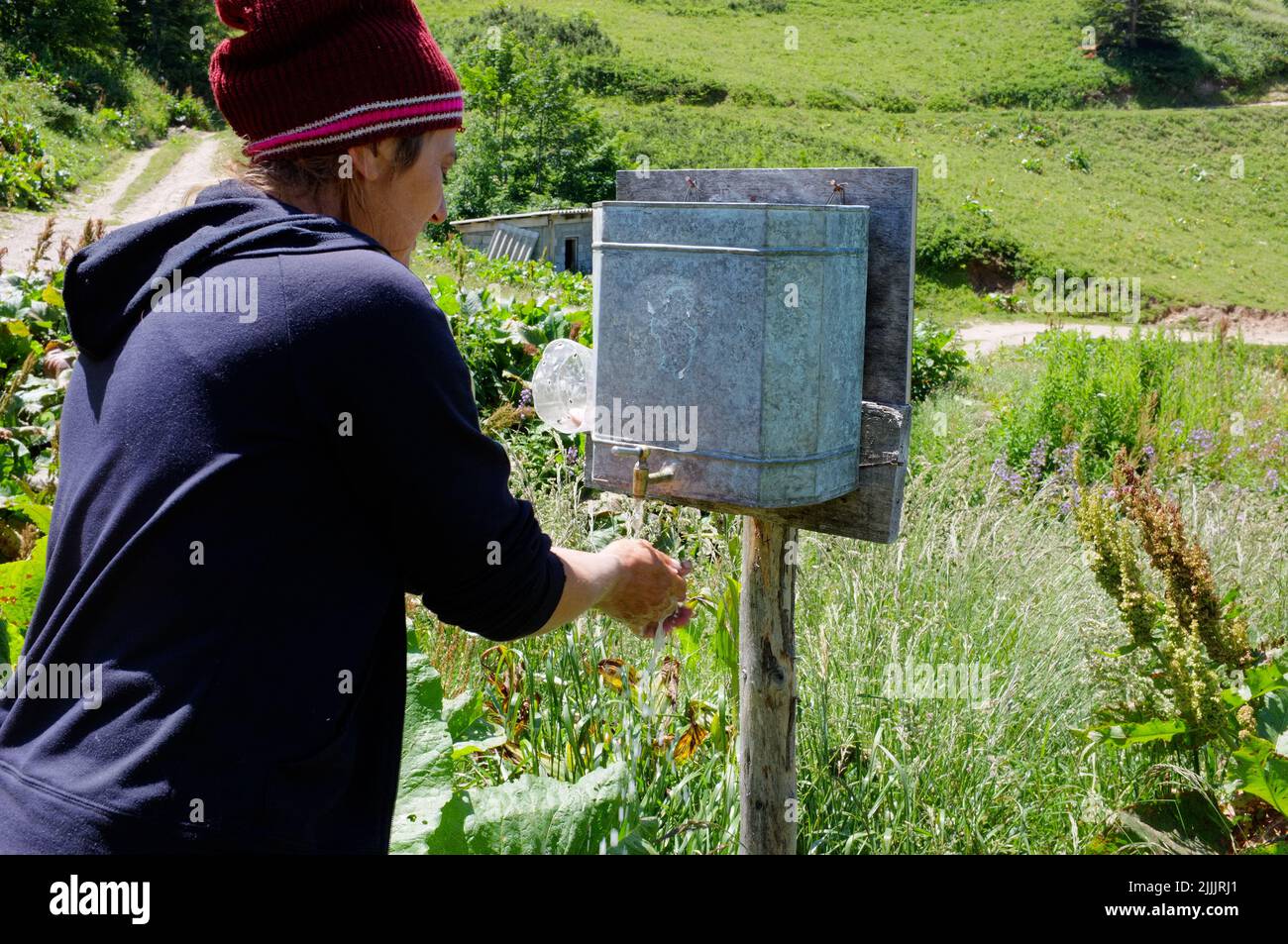 La donna montenegrina si sta lavando le mani dal dispenser di acqua in lamiera galvanizzata con rubinetto in ottone, il Parco Nazionale Biogradska Gora del Montenegro Foto Stock
