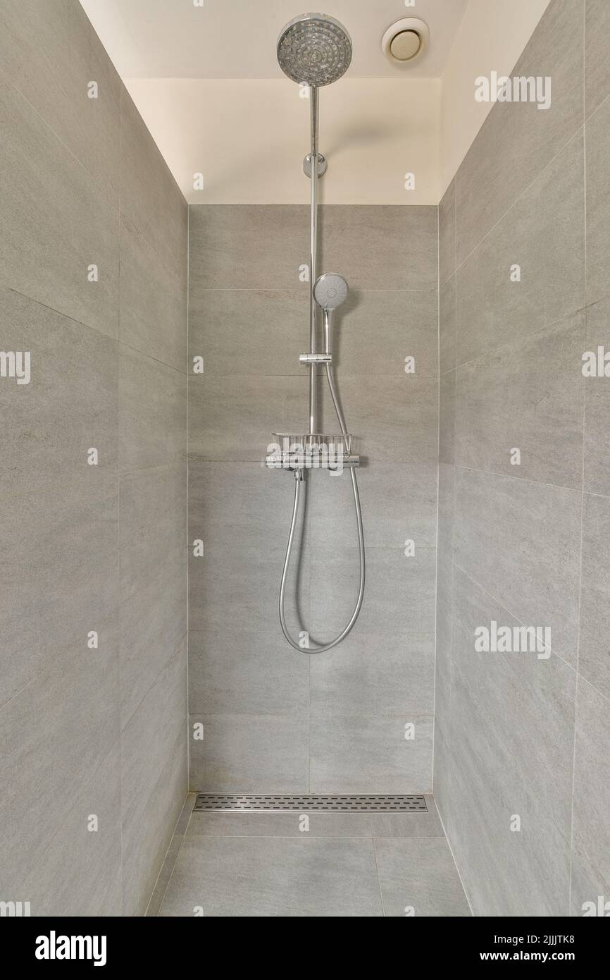 Moderna colonna doccia in un costoso bagno aperto con pareti e finestre in piastrelle grigie Foto Stock