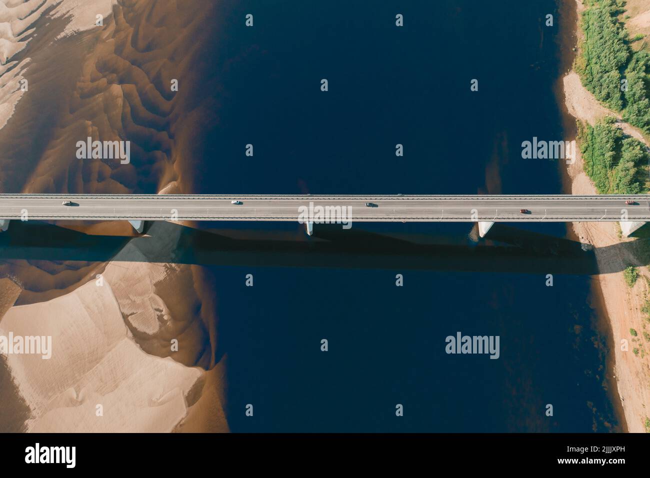 Un drone aereo ha girato delle automobili che guidano sul ponte sopra il fiume e sul lungofiume sabbioso al tramonto. Splendida vista dall'alto con una splendida costa con dune sabbiose. Ponte aereo drone con traffico auto Foto Stock