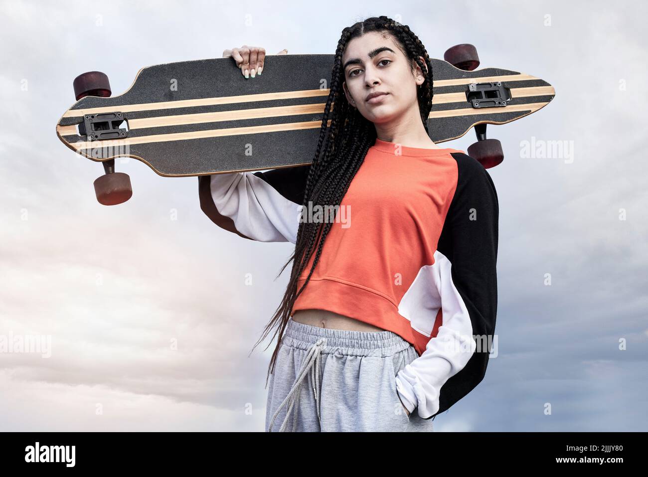 Sempre in su per un pattino. Ritratto corto di un attraente giovane skater femminile in piedi con la sua longboard contro uno sfondo tempestoso. Foto Stock