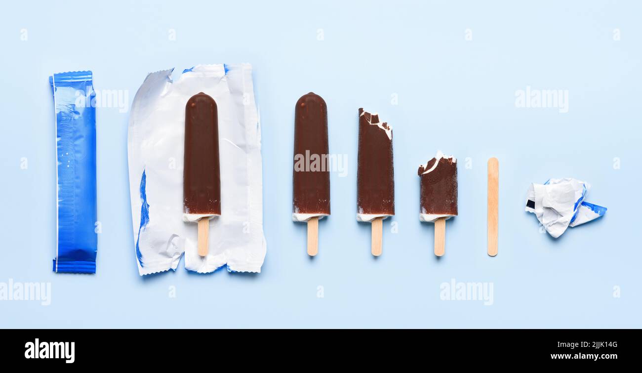 Gelato coperto di cioccolato su bastone di legno in diversi stati di consumo ciclo di vita su sfondo blu vista dall'alto piatto Foto Stock