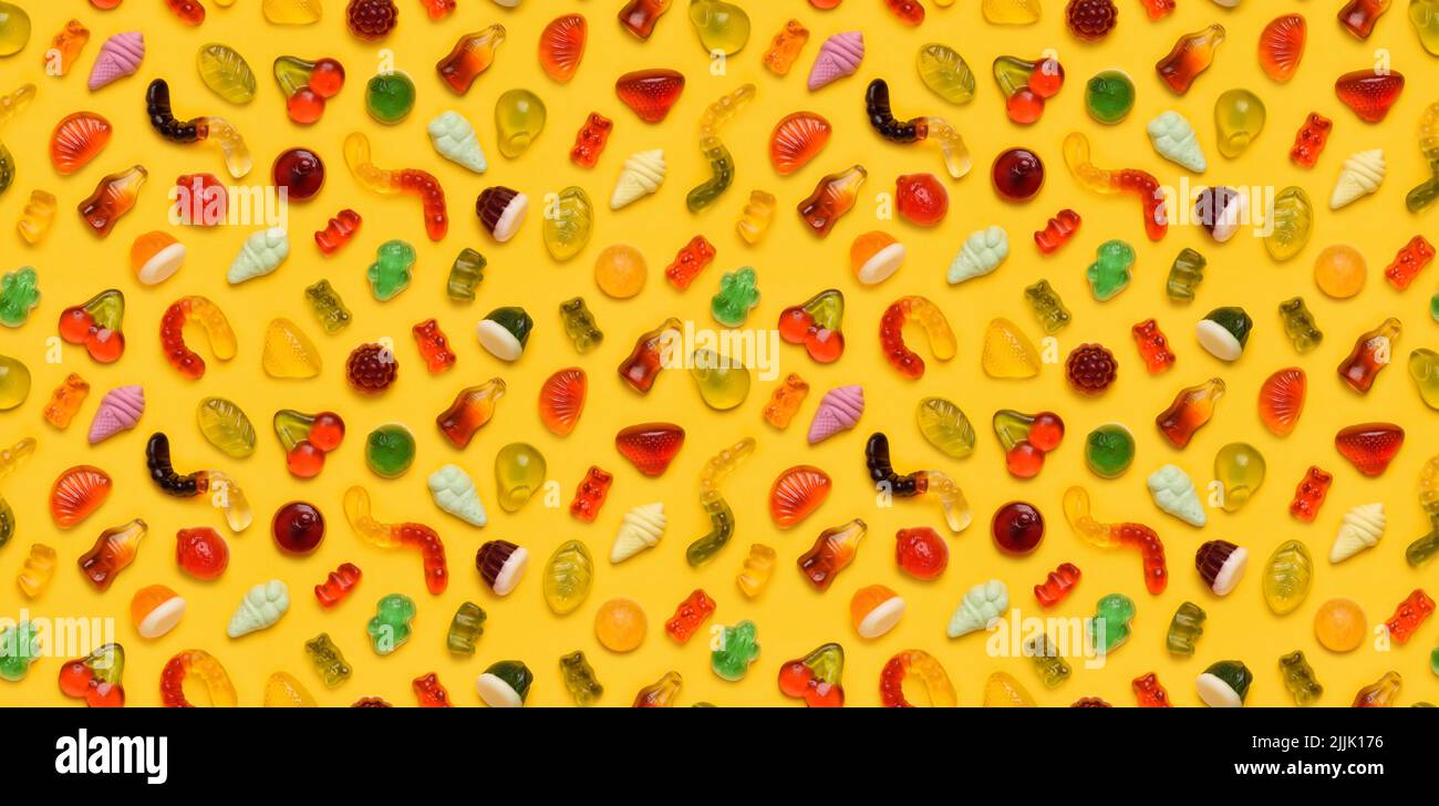 Modello senza cuciture di caramelle di frutta di gomma di gelatina assortite su sfondo giallo vista dall'alto posa piatta Foto Stock