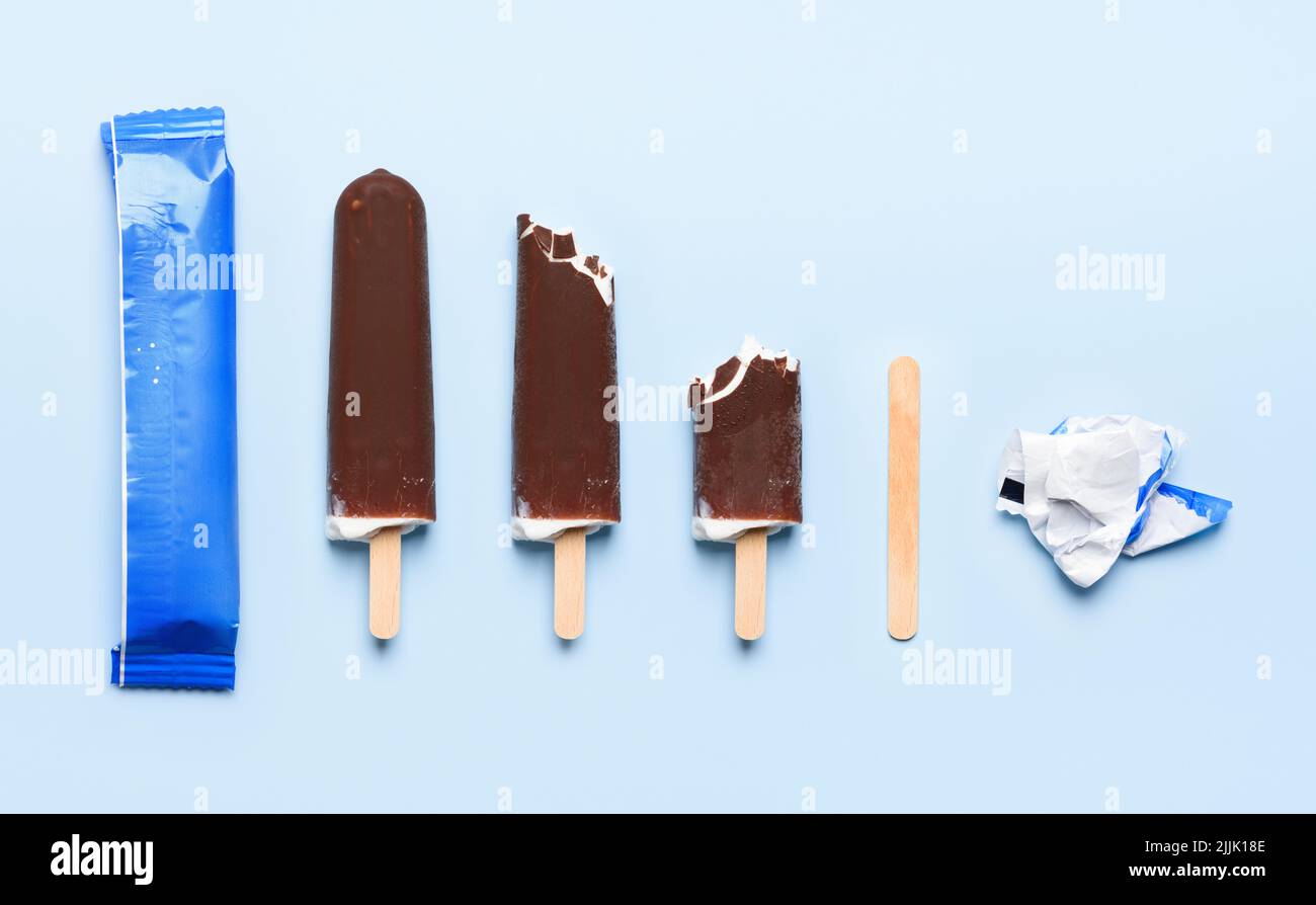 Gelato coperto di cioccolato su bastone di legno in diversi stati di consumo ciclo di vita su sfondo blu vista dall'alto piatto Foto Stock