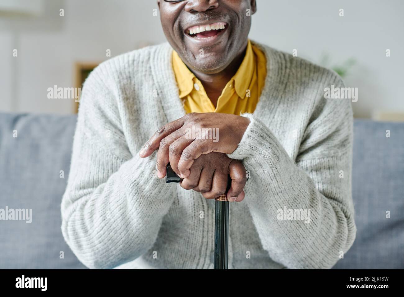 Primo piano dell'anziano africano appoggiato sul bastone seduto sul divano e sorridente Foto Stock