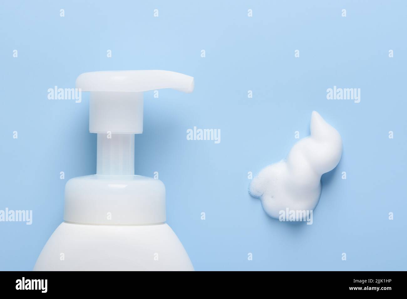 Flacone cosmetico bianco con dispenser a pompa e striscio in schiuma su sfondo blu, vista dall'alto, piatto Foto Stock