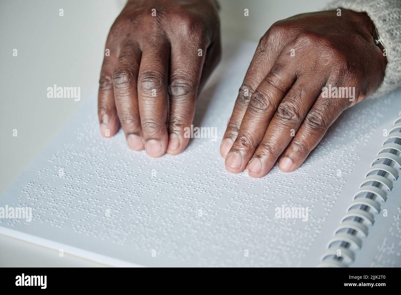 Alto angolo di visione dell'anziano africano che usa le sue mani per leggere il braille al tavolo Foto Stock