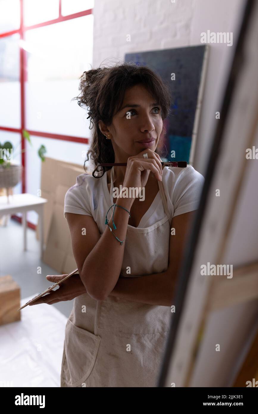Immagine verticale di una giovane artista biraciale che lavora su una nuova pittura in studio Foto Stock