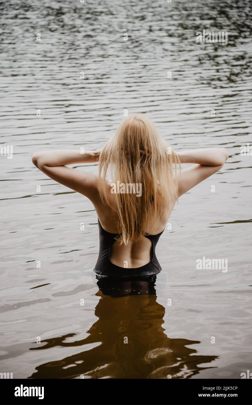 Giovane bella donna in piedi in acqua e fissando i capelli prima di nuotare. Calda serata estiva. Foto Stock