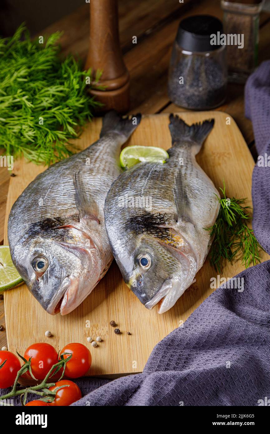 Pesce dorado sbucciato crudo con ingredienti da cucina. Pesce fresco su sfondo di legno. Foto Stock