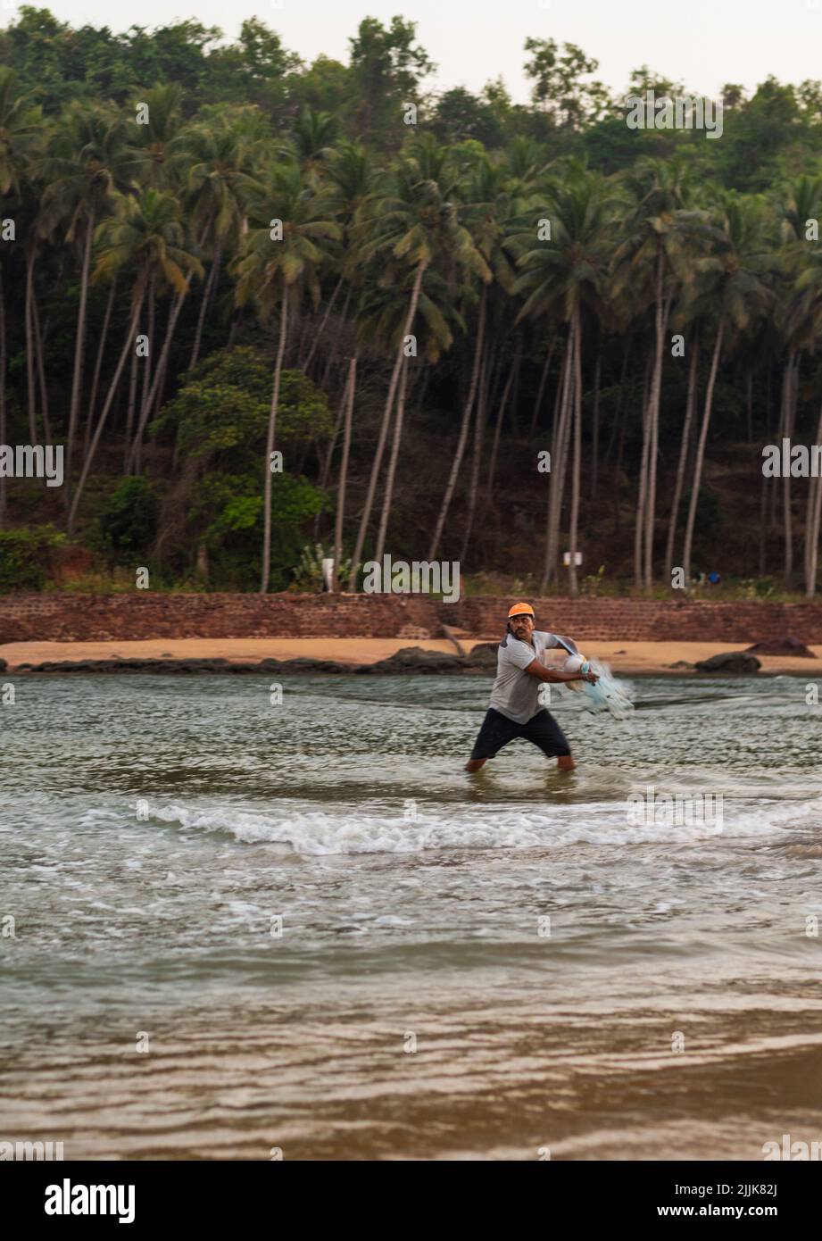 Un colpo verticale di un pescatore indiano locale gettando la rete nell'oceano a Betul, Salcete, Goa, India Foto Stock