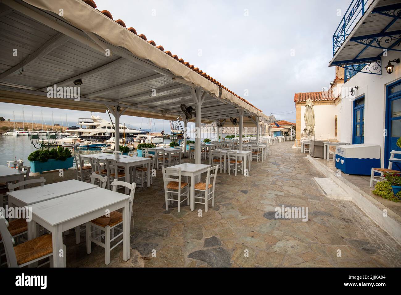 Un bar all'aperto con sedie e tavoli vuoti vicino al molo di Hydra, in Grecia Foto Stock