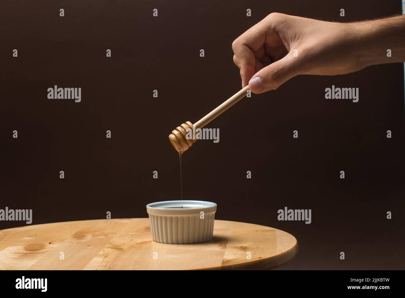 Sgocciolando il miele e un cucchiaio di legno sullo sfondo scuro Foto Stock