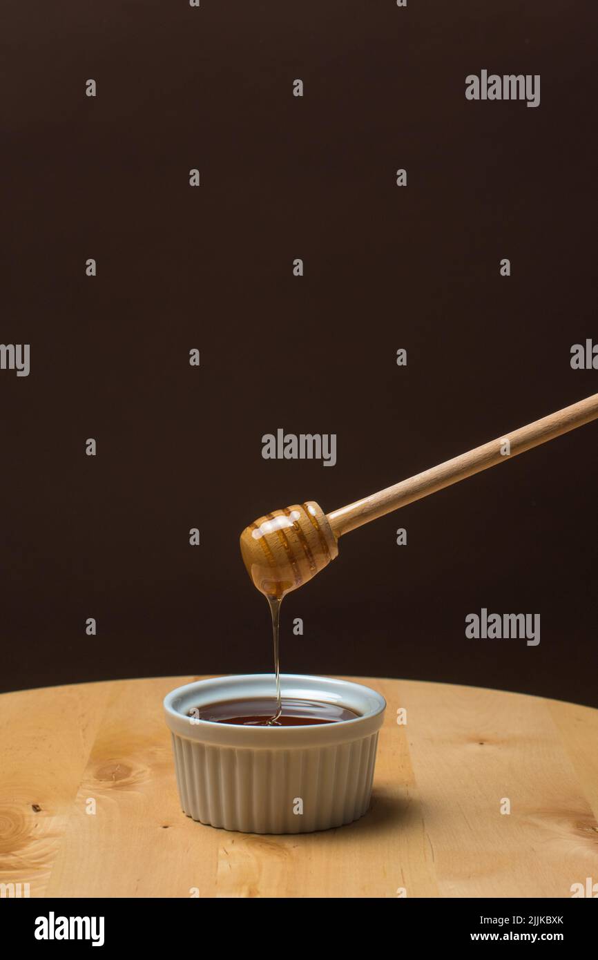 Una mano che tiene un cucchiaio di legno con il miele gocciolante Foto Stock