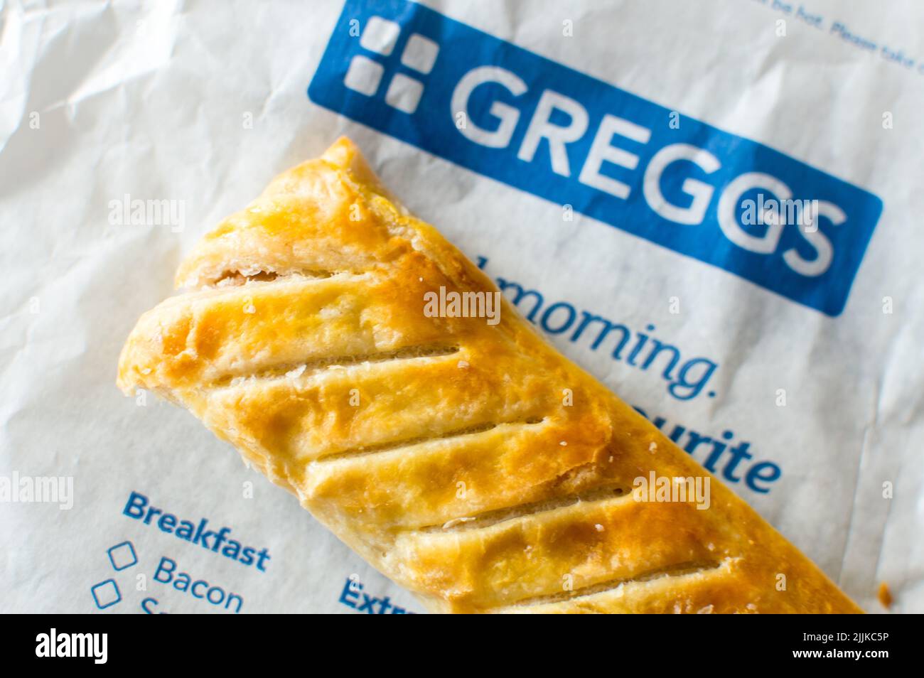 Il rotolo di salsiccia di Greggs è posto sopra un sacchetto di carta stampato di Greggs Foto Stock