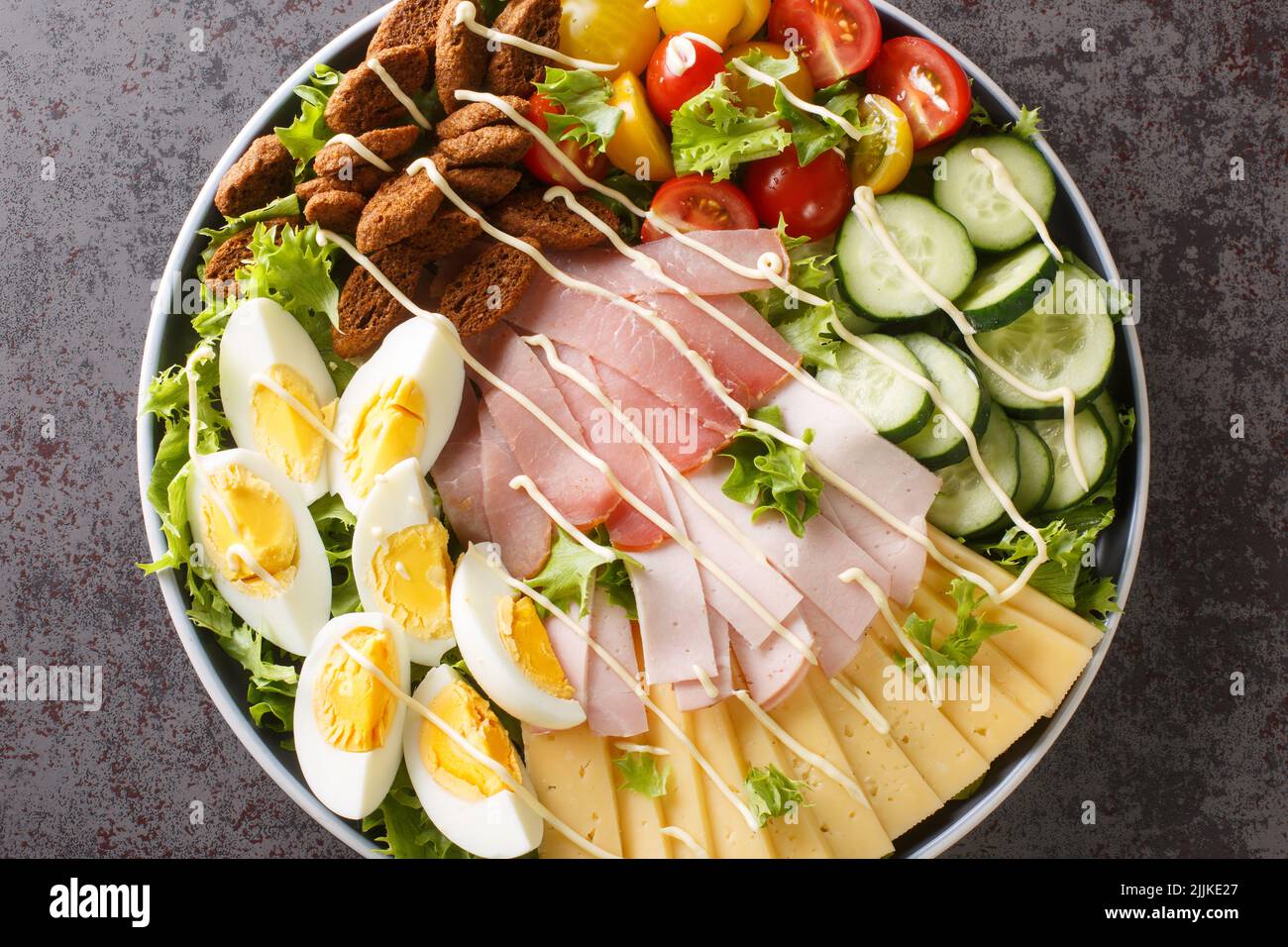 Deliziosa insalata dello chef composta da verdure, lattuga, uova, formaggio e diversi tipi di carne da vicino in un piatto sul tavolo. Vista orizzontale dall'alto f Foto Stock