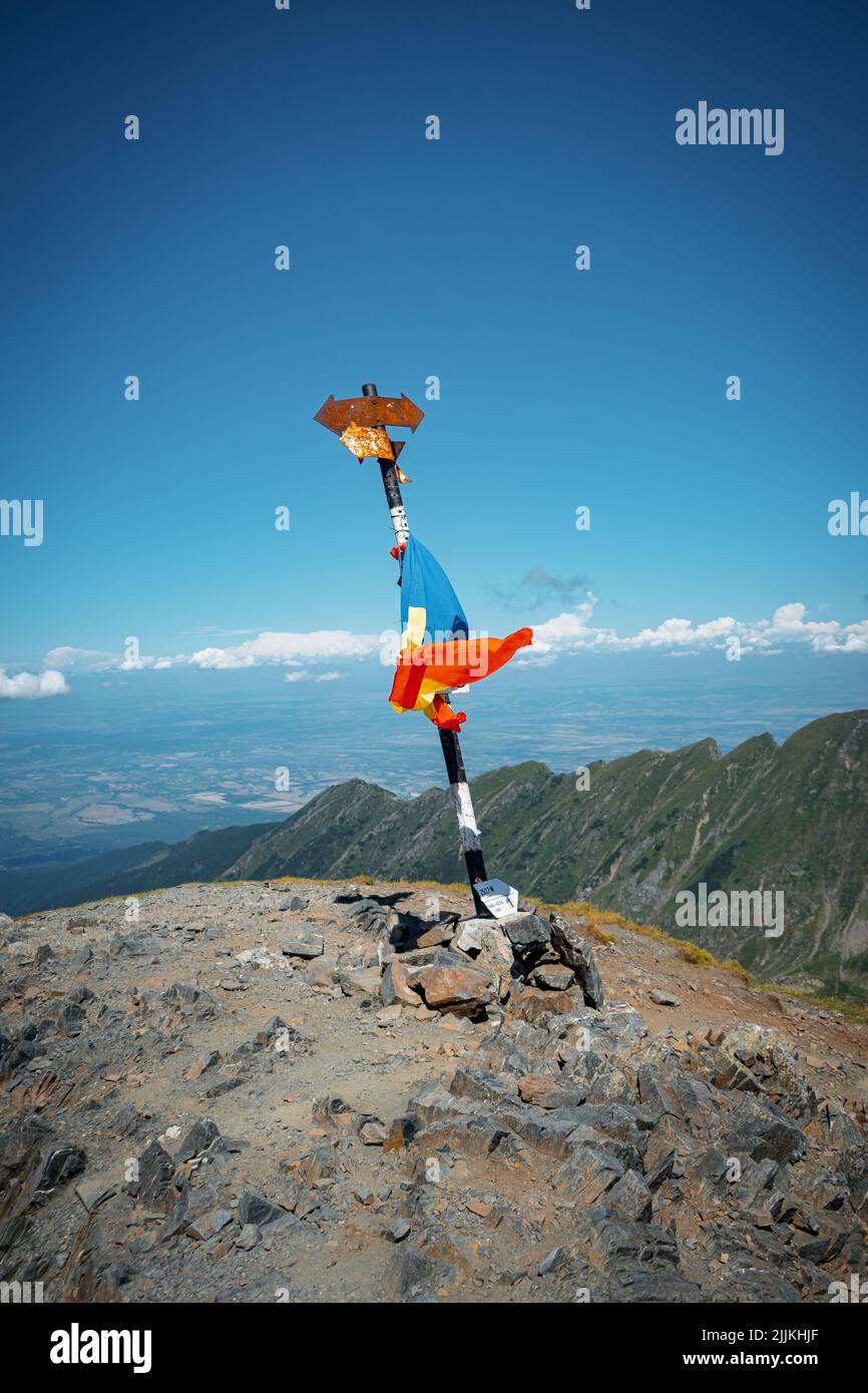 Un cartello di montagna in cima alle montagne e la bandiera rumena attaccata ad esso Foto Stock