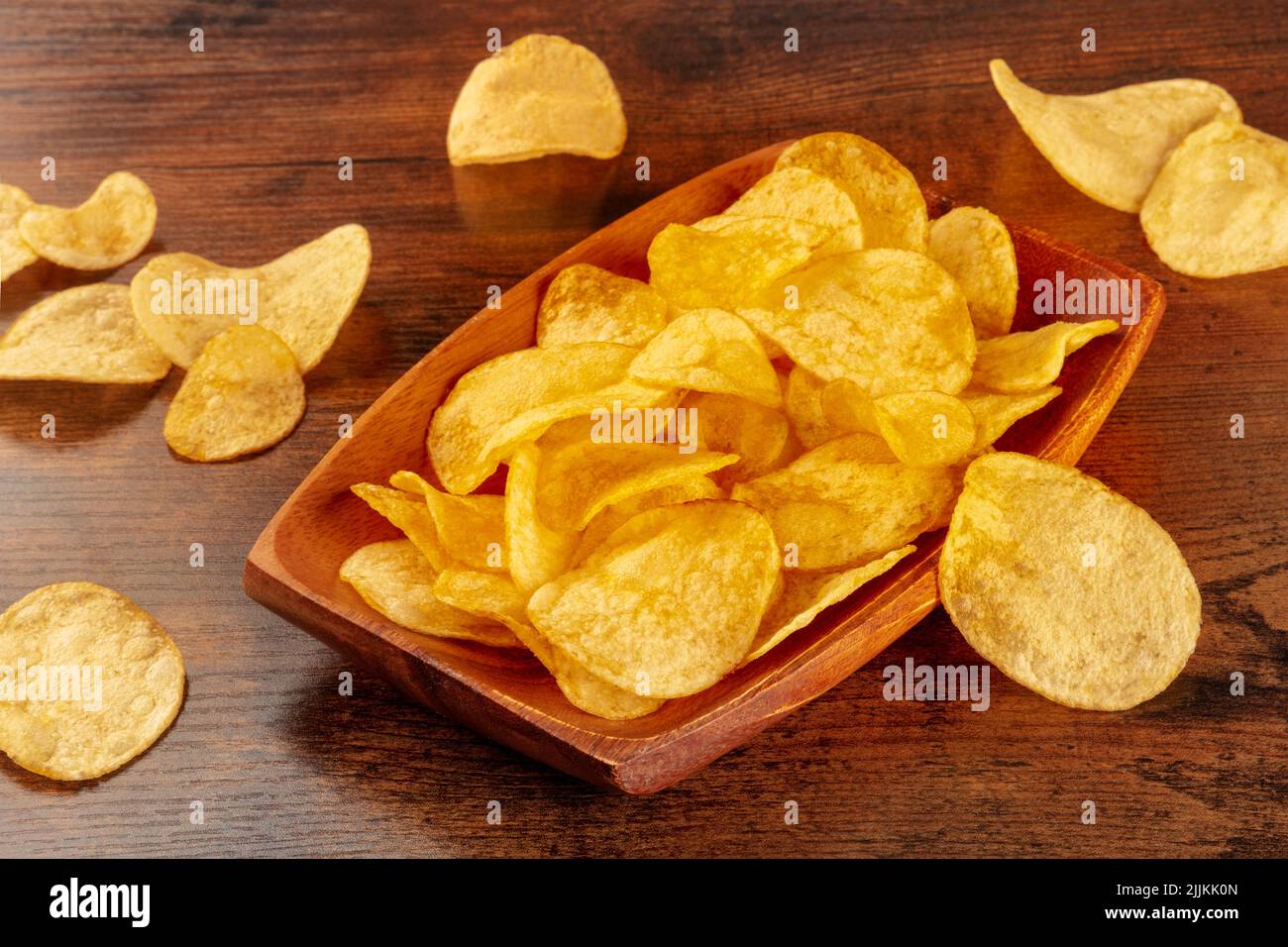 Patatine fritte o patatine in una ciotola e sparse su un tavolo di legno, uno spuntino salato Foto Stock