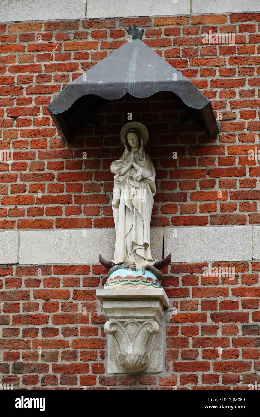 Un colpo verticale della statua della Vergine Maria contro un muro di mattoni rossi Foto Stock