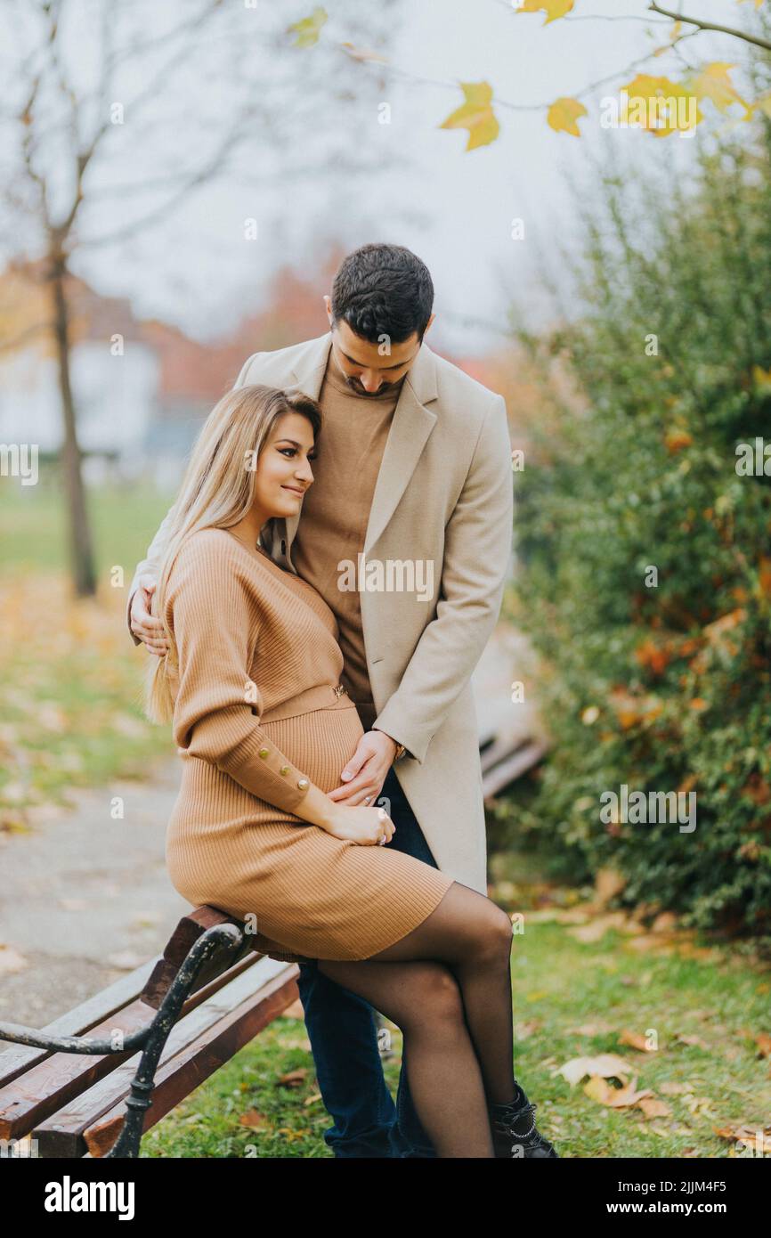 Una giovane donna incinta e suo marito appoggiati su una panca di legno Foto Stock